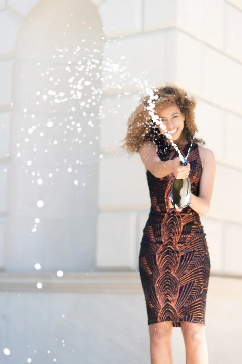 Claire Ofotokun (COFO) smiling as a celebratory bottle sprays across a vertical graduation portrait.
