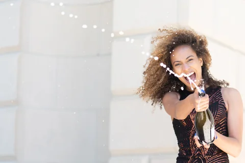 Claire Ofotokun (COFO) aiming a celebratory bottle toward the camera, with droplets crossing the frame.
