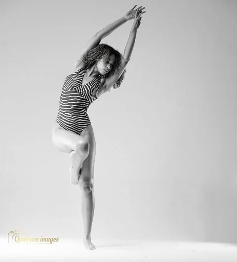 Black-and-white studio photograph of Claire Ofotokun (COFO) balancing on one leg with both arms extended overhead.