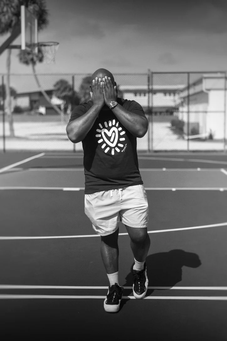 Black-and-white portrait of Gabriel on a basketball court with his hands covering his face.