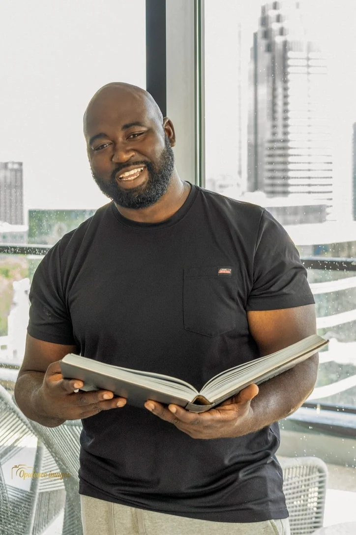 Gabriel smiling with an open book beside a window.