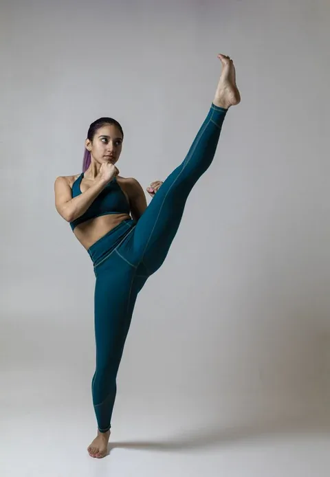 Athlete holding a high kick in teal activewear